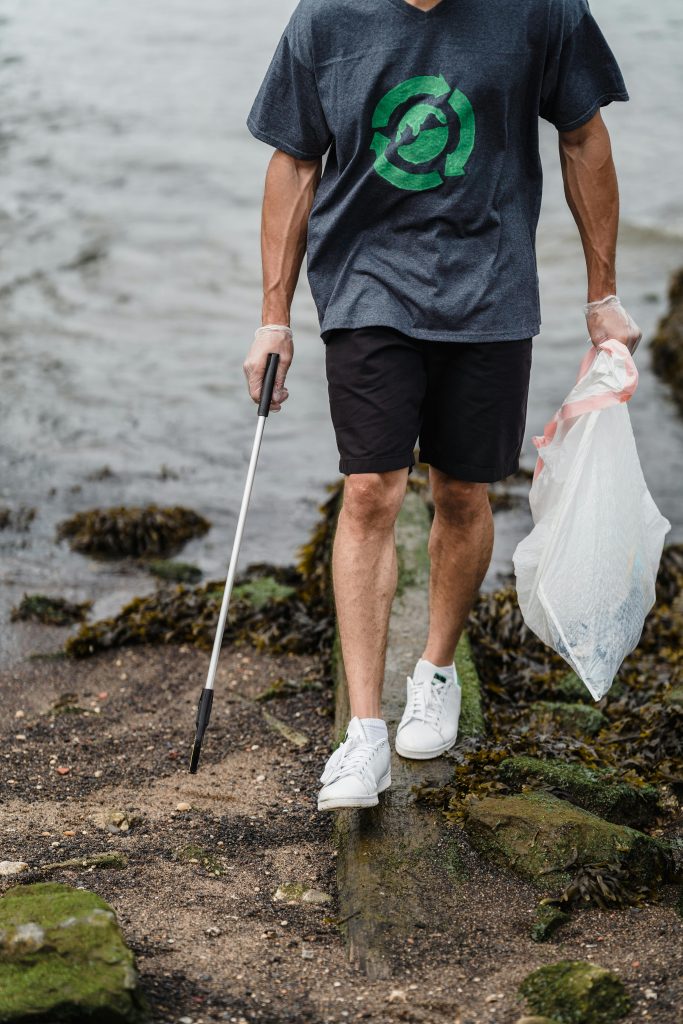 A man cleaning a beach, holding trash and a grabber tool highlighting environmental conservation.