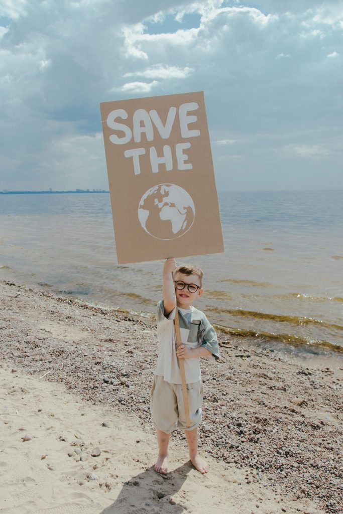 A child holding an environmental protest sign on a sandy beach.