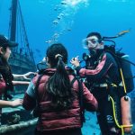 A dynamic scene depicting marine archaeologists and community volunteers working together underwater to document a shipwreck, symbolizing community collaboration in marine archaeology.