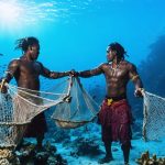 Indigenous Pacific Islander fishermen using traditional handmade nets, surrounded by a thriving coral reef, representing the integration of traditional knowledge in global marine conservation efforts.