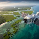 Satellite in low Earth orbit above a curving tropical coastline with vibrant mangrove forests, seagrass beds, and salt marsh mosaics in turquoise waters at golden hour, viewed at an oblique angle.