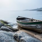 Foggy granite coastline with a small wooden boat resting on wet sand and a calm reflective sea in the distance.