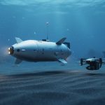 Underwater view of an autonomous torpedo-shaped glider and a compact drone hovering near coral in deep blue ocean water.