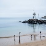 Coastal shoreline with a tide-gauge station near the rocks, ocean surface in the background, representing mean sea level measurement in maritime zones governance.