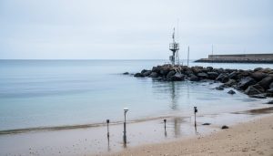 Coastal shoreline with a tide-gauge station near the rocks, ocean surface in the background, representing mean sea level measurement in maritime zones governance.