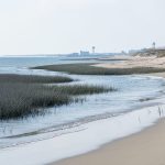 Virginia coastal marsh and dunes with seawater lapping at wet sand under an overcast sky, suggesting coastal inundation risk.